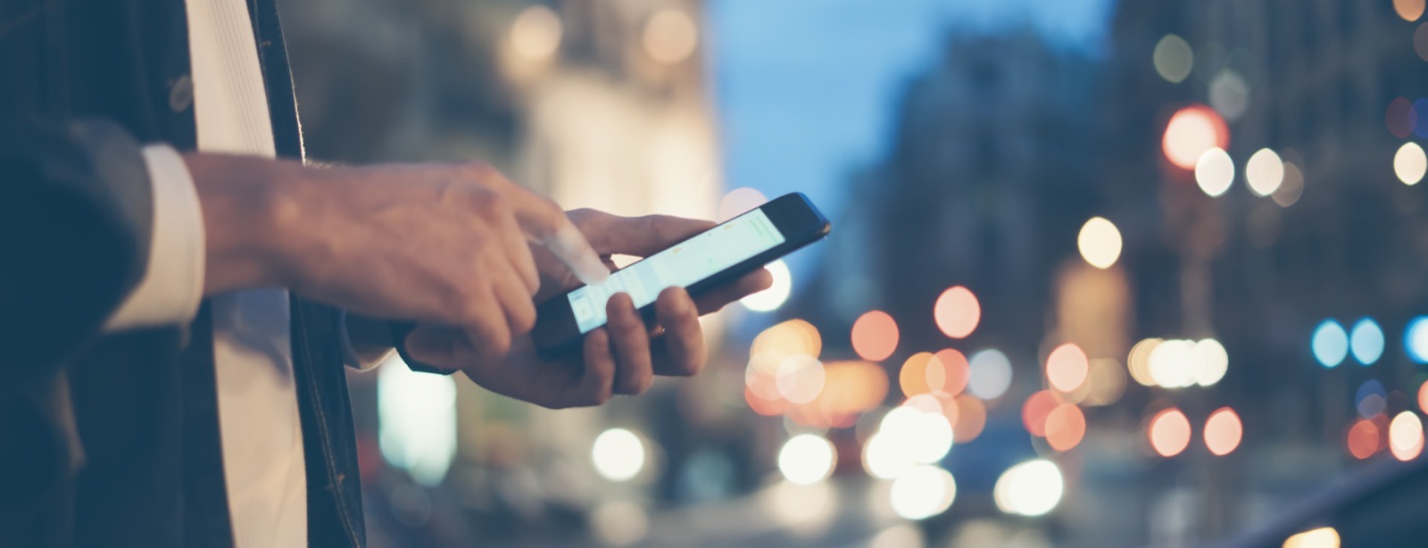 Customer typing a question into a smartphone on a city street at night, the exact moment AI optimization (AIO) is built to win